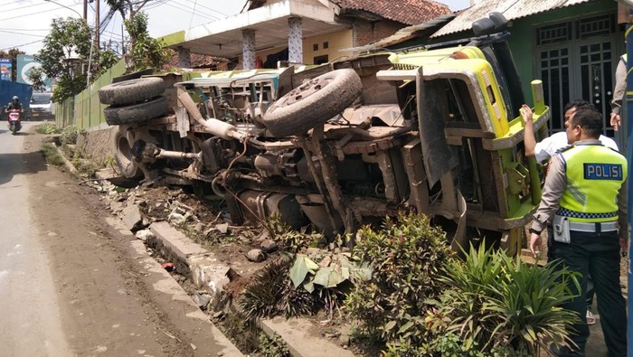 Truk bermuatan pasir terguling usai hantam jalan rusak. Muatan pasir menimpa rumah warga.