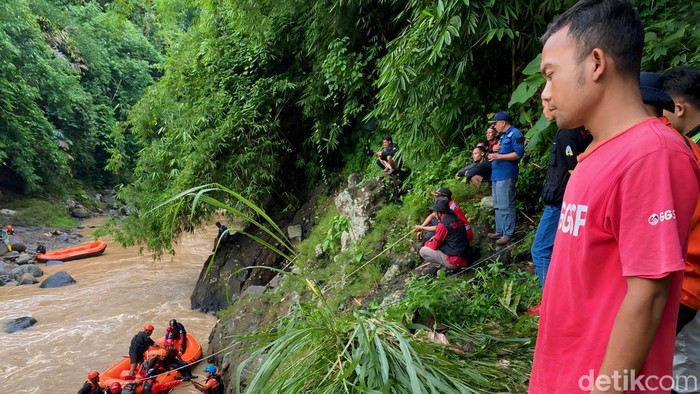 Erwin (baju merah) melihat pencarian Neneng, istrinya yang jatuh ke sungai.