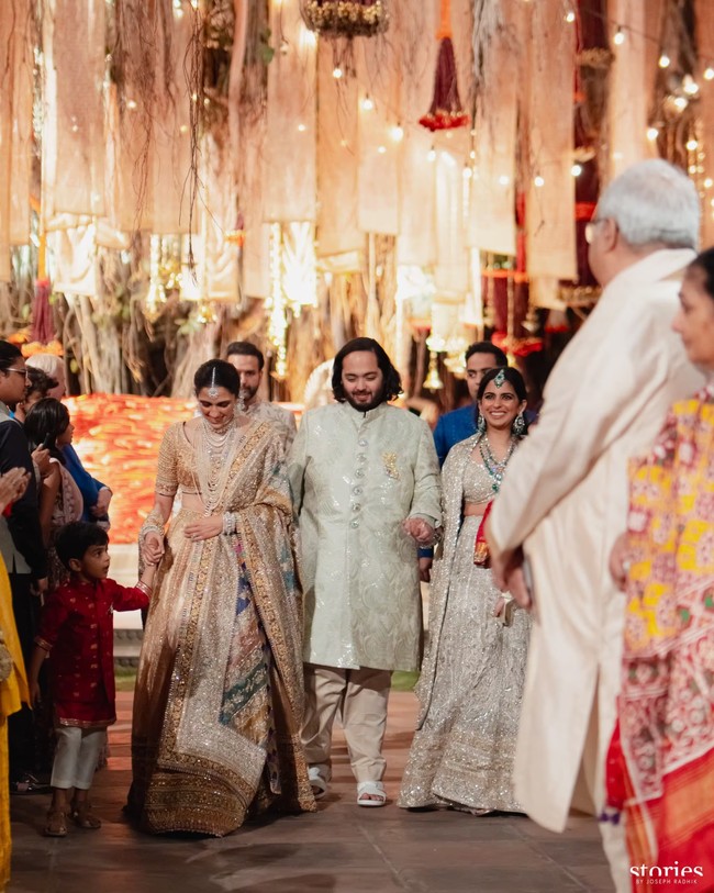 Saat memasuki podium, calon mempelai pria Anant Ambani terlihat gagah memakai sherwani berwarna putih gading. Putra bungsu Mukesh Ambani itu digandeng kakak perempuannya Isha Ambani dan istri dari abangnya Akash, Shloka Ambani. Foto: Instagram