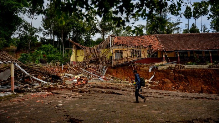 Seorang pewarta foto melintas di samping bangunan sekolah yang rusak dampak pergerakan tanah di Desa Cibedug, Kecamatan Rongga, Kabupaten Bandung Barat, Jawa Barat, Selasa (5/3/2024). Pusat Vulkanologi dan Mitigasi Bencana Geologi (PVMBG) memprediksi pergerakan tanah yang menghancurkan 10 rumah dan 192 kk mengungsi tersebut tidak akan meluas karena sudah terlokalisir dengan batas rekahan tanah yang berbentuk tapal kuda. ANTARA FOTO/Raisan Al Farisi/aww.