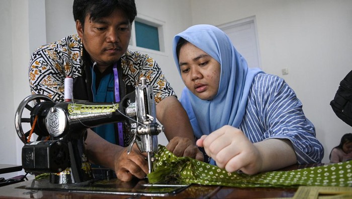 Pelatihan menjahit bagi penyandang disabilitas Orang tua memakaikan pakaian hasil pelatihan menjahit kepada anak penyandang disabilitas dengan didampingi seorang instruktur penyandang tuna daksa (kiri) di Gedung ABK UMKM, Tangerang Selatan, Banten, Rabu (6/3/2024). Pelatihan menjahit yang diikuti oleh anak penyandang disabilitas bersama orang tuanya tersebut dilakukan untuk meningkatkan keterampilan dan mengasah motorik melalui pemanfaatan kain bekas untuk dijadikan pakaian layak pakai. ANTARA FOTO/Sutlhony Hasanuddin/rwa.