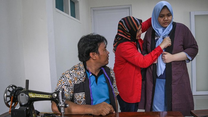 Orang tua memakaikan pakaian hasil pelatihan menjahit kepada anak penyandang disabilitas dengan didampingi seorang instruktur penyandang tuna daksa (kiri) di Gedung ABK UMKM, Tangerang Selatan, Banten, Rabu (6/3/2024).  Pelatihan menjahit yang diikuti oleh anak penyandang disabilitas bersama orang tuanya tersebut dilakukan untuk meningkatkan keterampilan dan mengasah motorik melalui pemanfaatan kain bekas untuk dijadikan pakaian layak pakai. ANTARA FOTO/Sutlhony Hasanuddin/rwa.