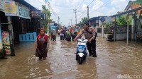 Anggota Samapta Polresta Mojokerto bantu dorong motor emak-emak yang mogok saat banjir di Kelurahan Meri, Kota Mojokerto.