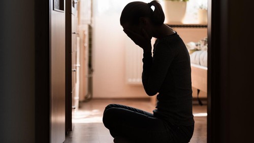 Sad young woman sitting on room floor crying with hand over face