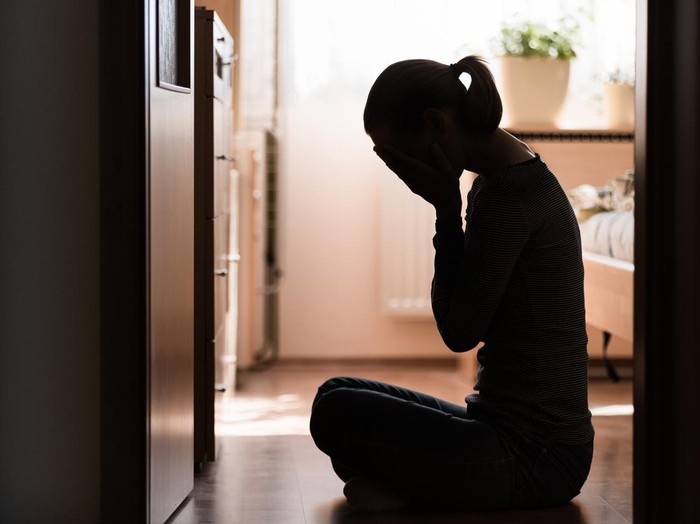 Sad young woman sitting on room floor crying with hand over face