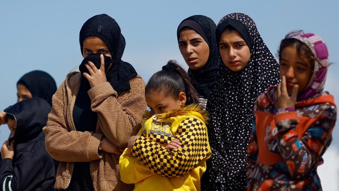 Women and children stand nearby while people bury the bodies of Palestinians killed in Israeli strikes and fire, after their bodies were released by Israel, amid the ongoing conflict between Israel and the Palestinian Islamist group Hamas, at a mass grave in Rafah, in the southern Gaza Strip, March 7, 2024. REUTERS/Mohammed Salem