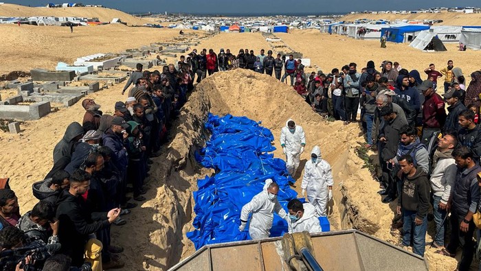 Women and children stand nearby while people bury the bodies of Palestinians killed in Israeli strikes and fire, after their bodies were released by Israel, amid the ongoing conflict between Israel and the Palestinian Islamist group Hamas, at a mass grave in Rafah, in the southern Gaza Strip, March 7, 2024. REUTERS/Mohammed Salem