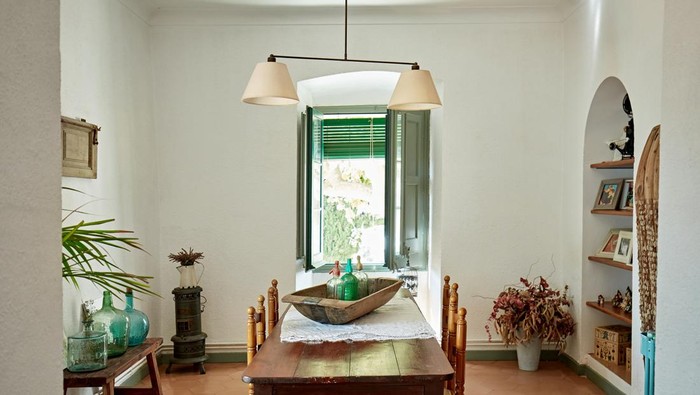 View through archway into dining room with vintage table for four, hanging light fixture, knick knacks, and terracotta tile flooring.