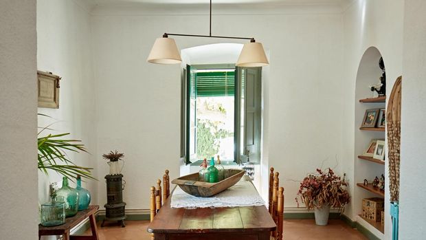 View through archway into dining room with vintage table for four, hanging light fixture, knick knacks, and terracotta tile flooring.