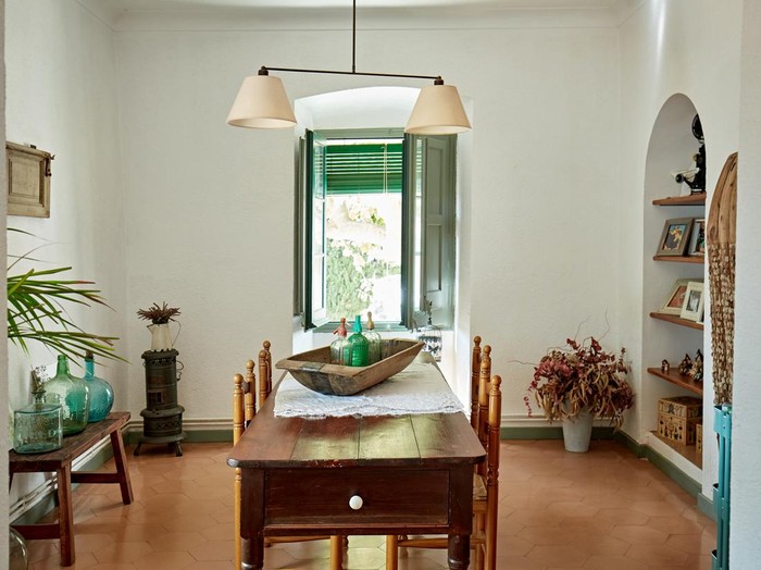 View through archway into dining room with vintage table for four, hanging light fixture, knick knacks, and terracotta tile flooring.