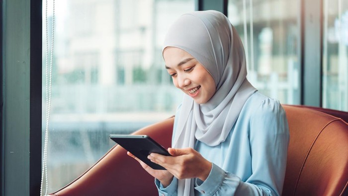 Ilustrasi perempuan berhijab menggunakan ponsel atau tab