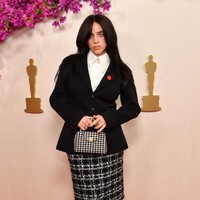 Billie Eilish tampil dengan busana dan aksesori yang semuanya dari brand Chanel. Dia mengenakan rok tweed khas Chanel yang dipadukan dengan blazer hitam dan kemeja berkerah dengan kancing.  Foto: WireImage/Sarah Morris
