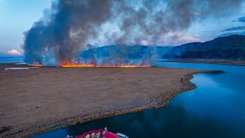 TRAVEL Yan Li (China) berjudul Between Calm and Catastrophe, sebuah gambar desa terapung yang tenang berdiri di tepi Danau Titicaca yang tenang, kontras dengan bahaya kebakaran hutan di daratan di dekatnya. Foto: Sony World Photography