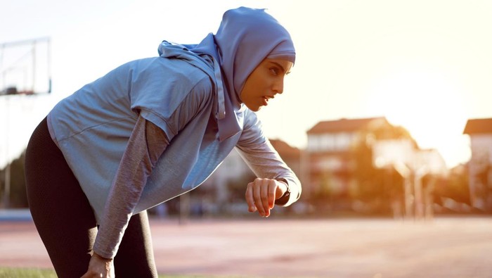 Tired Muslim woman, an track and field athlete measuring her pulse trace with a fitness tracker, after she finishes with training