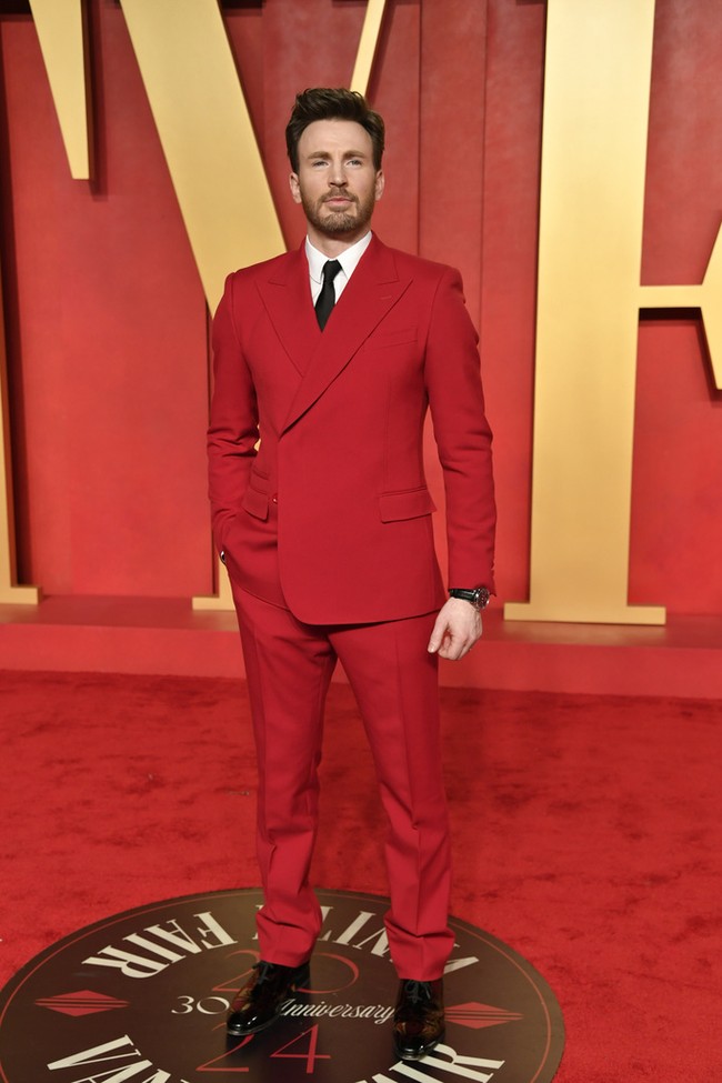 Chris Evans tampil ‘serasi’ dengan karpet merah dalam setelan jas merah dari koleksi Dolce & Gabbana. Jas model double-breasted itu dipasangkan dengan kemeja putih dan dasi sutera hitam. Foto: Evan Agostini/Invision/AP