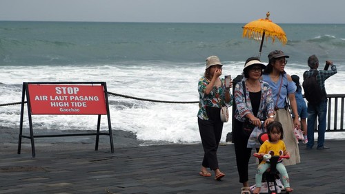 Wisatawan berjalan di dekat papan larangan di objek wisata Tanah Lot, Tabanan, Bali, Kamis (14/3/2024). Badan Meteorologi, Klimatologi, dan Geofisika (BMKG) Wilayah III Denpasar memprediksi terjadinya cuaca ekstrem di wilayah Bali selama tiga hari pada 14-16 Maret 2024 yang merupakan dampak dari terbentuknya bibit siklon tropis 91S dan 94S di wilayah Indonesia. ANTARA FOTO/Nyoman Hendra Wibowo/rwa.