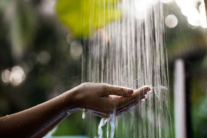 Close up of unrecognizable woman holding her hands under the shower during summer day in nature.