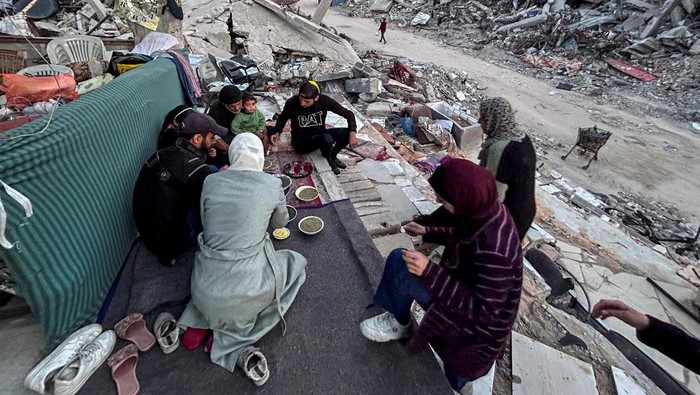Potret Warga Gaza Berbuka Puasa di Antara Puing-puing Bangunan Palestinian members of Al-Khlout family break their fast on the rubble of their house which was destroyed during Israel's military offensive, during the holy month of Ramadan, as the conflict between Israel and Hamas continues, in Beit Lahia in the northern Gaza Strip, March 13, 2024. REUTERS/Mahmoud Issa