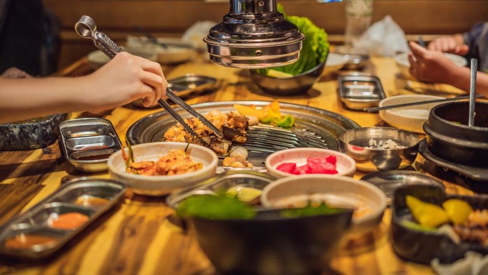 Excited Asian woman holding a camera while tasting food and introducing a Korean restaurant.