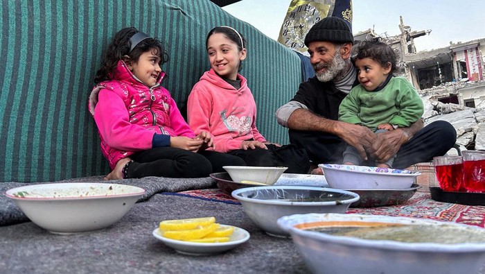 Palestinian members of Al-Khlout family wait to break their fast on the rubble of their house which was destroyed during Israel's military offensive, during the holy month of Ramadan, as the conflict between Israel and Hamas continues, in Beit Lahia in the northern Gaza Strip, March 13, 2024. REUTERS/Mahmoud Issa