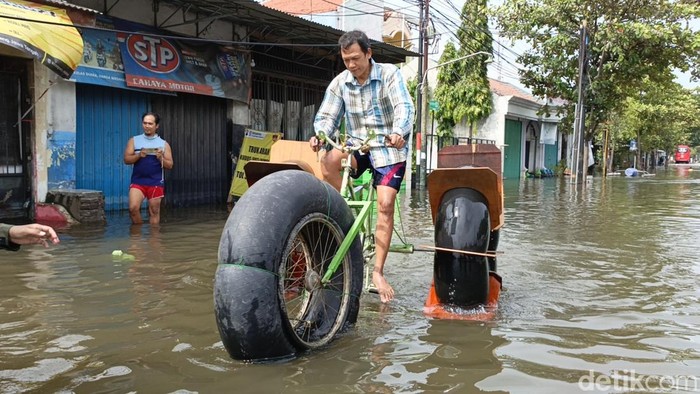 Tasin (51) tampak menjajal sepeda air buatannya di tengah banjir di depan rumahnya di Jalan Raya Kaligawe, Semarang, Jumat (15/3/2024).