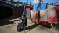 Seorang wanita Palestina membaca Al-Quran di dekat kamp pengungsi, pada hari kedua bulan suci Ramadhan, di Deir al-Balah di Jalur Gaza tengah pada 12 Maret 2024. Majdi Fathi/NurPhoto via Getty Images. 