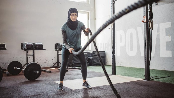 Young woman on cross training exercising with battle rope. Wearing sports clothing and hijab.
