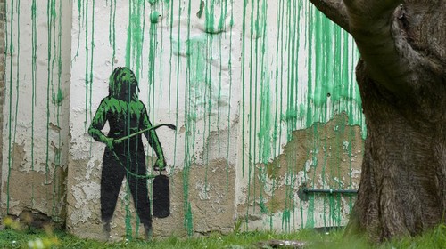 A woman takes a picture on her phone of a new Banksy painting on a wall in London, Monday, March 18, 2024. A new Banksy mural drew crowds to a London street on Monday, even before the elusive graffiti artist confirmed that the work was his. The artwork in the Finsbury Park neighborhood covers the wall of a four-story building and shows a small figure holding a pressure hose beside a real tree. Green paint has been sprayed across the wall, replicating the absent leaves of the tree, which has been severely cropped. Banksy claimed the work by posting before and after photos of the location on his official Instagram account.(AP Photo/Alastair Grant)