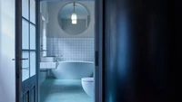 Pada bagian kamar mandi dipilih warna-warna cool tone dengan ubin putih dan cermin besar untuk mencerahkan ruangan. Di kamar mandi tersebut sudah ada bathtub, toilet duduk, cermin, dan wastafel. Foto: BoysPlayNice via Dezeen