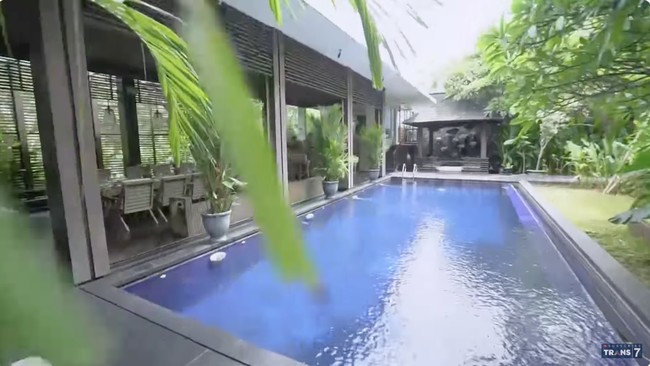 Halaman belakang difungsikan untuk kolam renang dan tempat untuk bersantai. Pepohonan rindang, salah satunya sudah berusia ratusan tahun yang didatangkan langsung dari Bali, makin meneduhkan suasana. (Foto: YouTube/Trans7 Official)