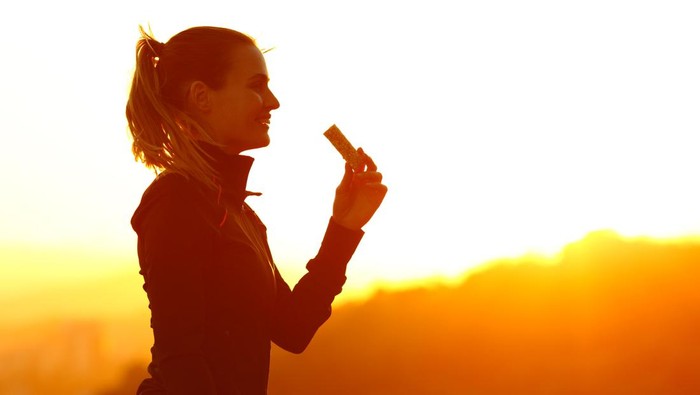 Silhouette of runner woman eating energy bar after running at sunset in the mountain