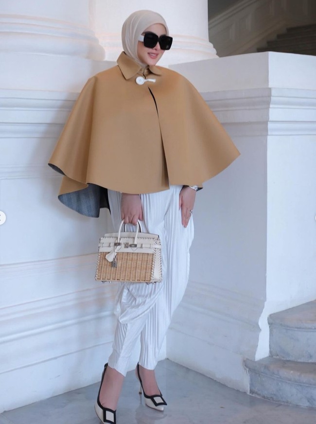Di unggahan terbaru akun Instagram pribadinya Syahrini tampak memadukan outer cape berwarna coklat dengan celana putih plisket. Penampilannya itu kemudian dilengkapi dengan hijab berwarna coklat, sepasang heels, dan kaca mata hitam. Foto: Instagram/@princessyahrini