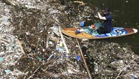 Seorang relawan yang duduk di papan dayung memungut sampah di sungai Pecatu, Bali, Indonesia pada Jumat, 22 Maret 2024. 