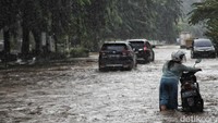Seorang warga mendorong sepeda motornya yang mogok akibat banjir.  