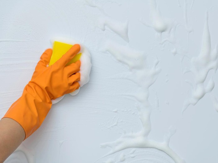 Woman hand cleaning blue wall with sponge.