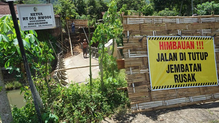 Warga menyeberangi jembatan yang ambrol tergerus banjir di Desa Kalidawir, Tulungagung, Jawa Timur, Minggu (24/3/2024). Pondasi di kedua sisi/ujung jembatan penghubung desa itu amblas tergerus luapan air yang membanjiri daerah itu sehingga menyebabkan badan jembatan patah dan turun sekitar 50 centimeter sehingga tidak bisa dilalui kendaraan. ANTARA FOTO/Destyan Sujarwoko/aww.