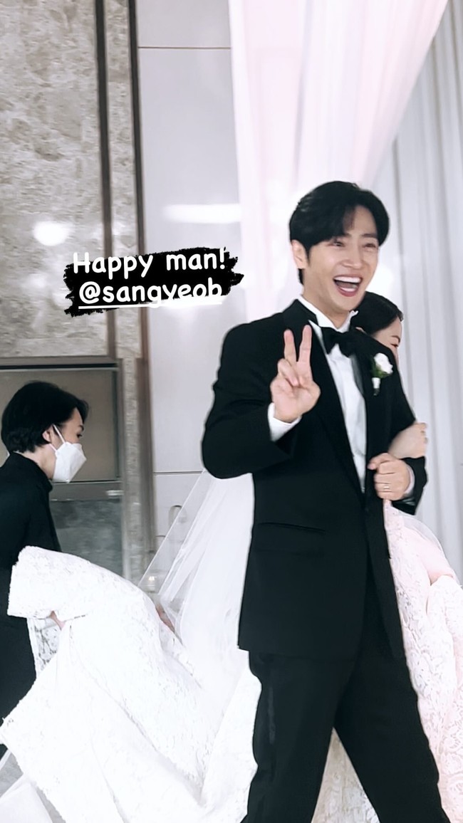 Di hari pernikahannya, Lee Sang Yeob tampil gagah memakai setelan jas hitam. Sedangkan istrinya tampil anggun dalam balutan gaun putih dan veil. Aura bahagia terpancar dari wajah Lee Sang Yeob saat menggandeng istrinya, melewati altar. Foto: dok. Instagram @all_for_yeob