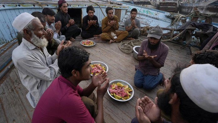 Momen Kebersamaan Nelayan Pakistan Buka Puasa di Atas Kapal Pakistani fishermen pray before breaking their fast at a boat in the fish harbor on the Arabian Sea during the Muslim's holy fasting month of Ramadan, in Karachi, Pakistan, Sunday, March 24, 2024. (AP Photo/Fareed Khan)