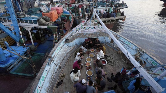 Momen Kebersamaan Nelayan Pakistan Buka Puasa di Atas Kapal Pakistani fishermen pray before breaking their fast at a boat in the fish harbor on the Arabian Sea during the Muslim's holy fasting month of Ramadan, in Karachi, Pakistan, Sunday, March 24, 2024. (AP Photo/Fareed Khan)