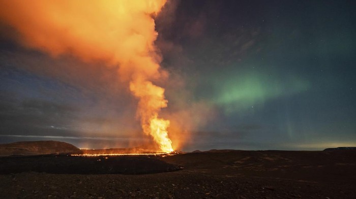 A view of the lava flowing from the volcano backdropped by the Northern Lights, near the town of Grindavik, Iceland, early Saturday, March 23, 2024.  The volcano in southwestern Iceland that erupted three times in December, January and February, sending lava towards a nearby community, keeps erupting. (AP Photo/Marco di Marco)