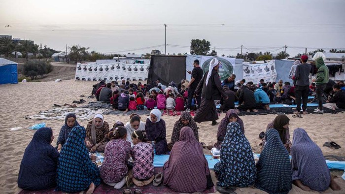Potret Pengungsi Palestina Berbuka Puasa Bersama RAFAH, GAZA - MARCH 27: Displaced Palestinians gather to break their fast at a communal table set up amidst the tents as mass iftar dinner organized for displaced Palestinians in Rafah, Gaza on March 27, 2024. Israeli attacks from the air, sea, and land on the Gaza Strip persist. Despite the ongoing Israeli attacks, a mass iftar program was arranged for Palestinian families who were forced to flee their homes due to the Israeli attacks and sought refuge in Rafah city within Gaza, where they reside in tents. (Photo by Jehad Alshrafi/Anadolu via Getty Images)