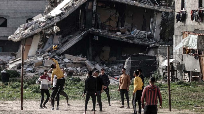 Warga Gaza Bermain Voli di Samping Reruntuhan Bangunan DEIR AL-BALAH, GAZA - MARCH 27: Palestinian youths, who take refuge in Nuseirat camp from ongoing Israeli attacks, pass the time by playing volleyball near a partially collapsed building while waiting for iftar time on the Holy month of Ramadan in Deir al-Balah, Gaza on March 27, 2024. (Photo by Ali Jadallah/Anadolu via Getty Images)
