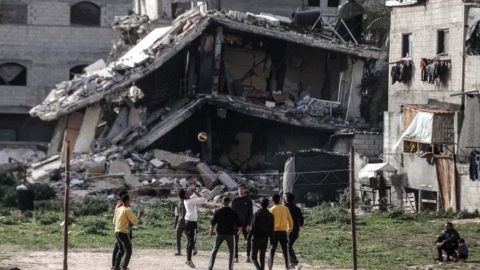 Warga Gaza Bermain Voli di Samping Reruntuhan Bangunan DEIR AL-BALAH, GAZA - MARCH 27: Palestinian youths, who take refuge in Nuseirat camp from ongoing Israeli attacks, pass the time by playing volleyball near a partially collapsed building while waiting for iftar time on the Holy month of Ramadan in Deir al-Balah, Gaza on March 27, 2024. (Photo by Ali Jadallah/Anadolu via Getty Images)