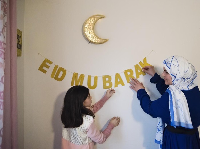 1492704677 North-American muslim mother and daughter decorating home for Ramadan. Girl is wearing a traditional moroccan dress, mother is wearing a hijab. Horizontal waist up indoors shot with copy space. This was taken in Quebec, Canada.