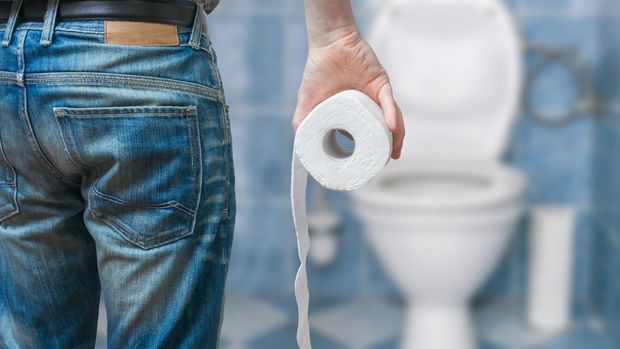 Man suffers from diarrhea holds toilet paper roll in front of toilet bowl.