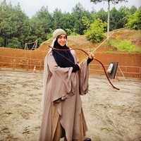 Selain berdakwah, Haneen juga menyalurkan hobi memanah. Haneen berpose dengan busur dan anak panah. Haneen memakai dress warna cokelat dipadu dengan hijab syari hitam. Foto: Dok. Instagram @haneenakira.
