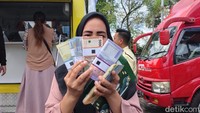 Seorang warga yang sudah mendapatkan uang baru tampak berpose. Ia berpose menutup separuh wajahnya dengan uang baru.