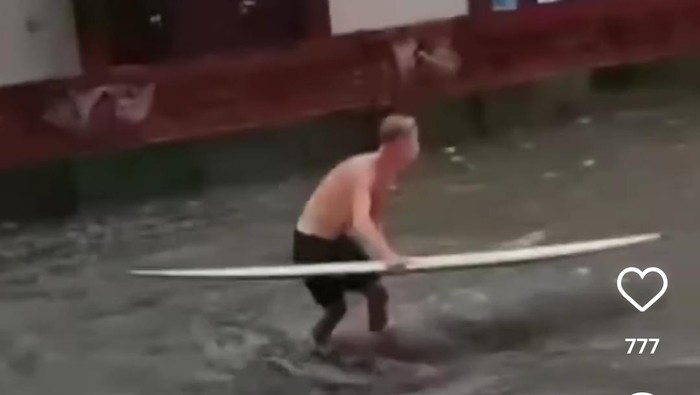 Bule bermain papan surfing di Jalan Pantai Kuta saat banjir, Kamis.