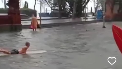 Bule bermain dengan papan surfing saat banjir di Jalan Pantai Kuta, Kamis (4/4/2024).