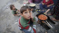 Anak-anak Palestina menunggu di samping api unggun saat orang-orang menyiapkan makanan untuk berbuka puasa di Deir Al Balah, Gaza, 3 April 2024. 